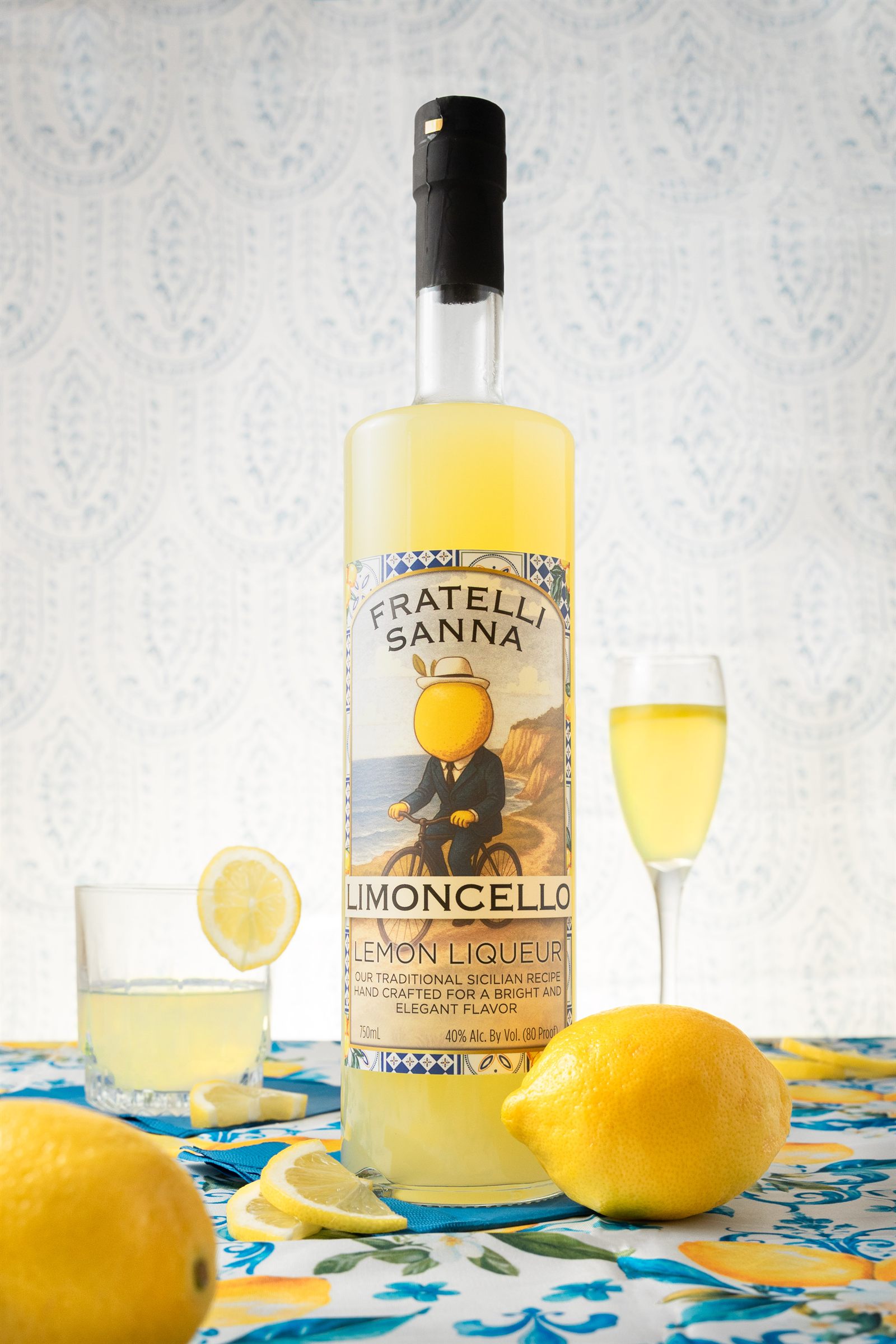 A bottle of Fratelli Sanna Limoncello with fresh lemons on a Sicilian tablecloth